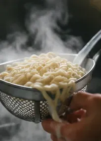 台所で麺を湯切りする手元